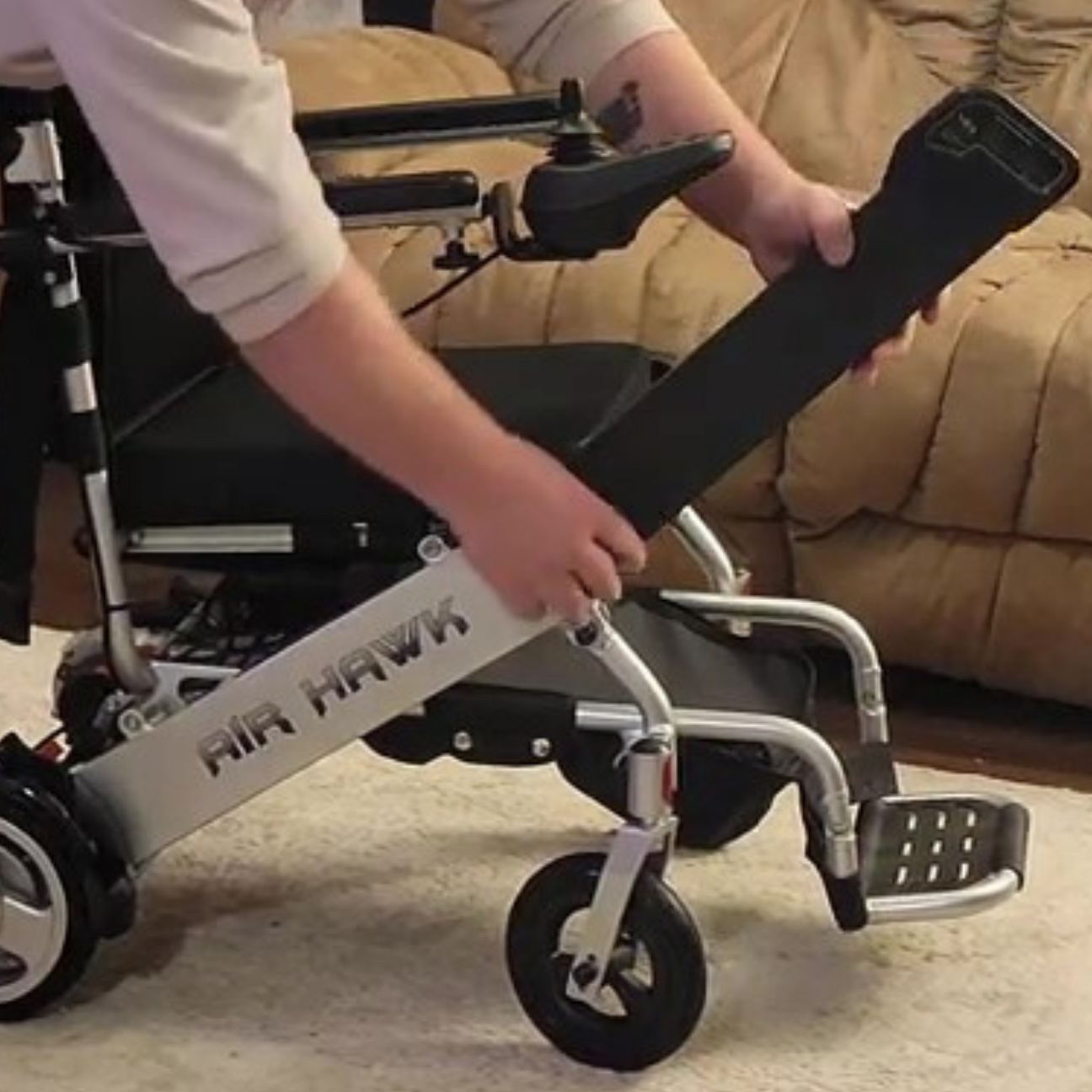 Air Hawk electric wheelchair with a man's hand demonstrating how to remove the battery.